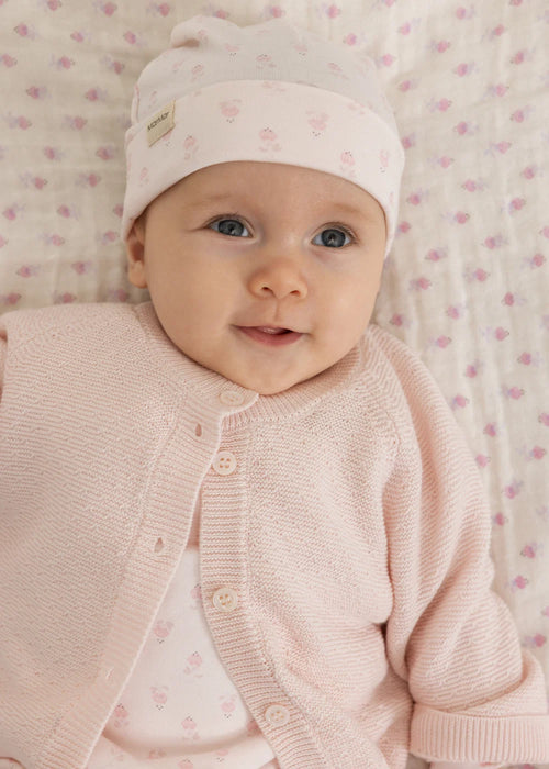Boxpakje met voetjes – Rubetta Mini Bloom – MarMar Copenhagen: baby draagt de lichtroze babymuts in een verschoonmand.