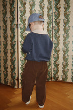 Polo en laine Basi – Dark Blue Stripe – Konges Sløjd : enfant portant le polo bleu et un pantalon marron, de dos.